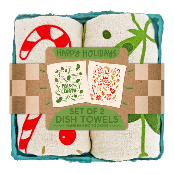 The Neighborgoods Dish Towel Set of 2 - Happy Holidays features festive cotton towels with candy cane and mistletoe designs, rolled in a box adorned with illustrated holiday cards—an ideal kitchen gift for the season.