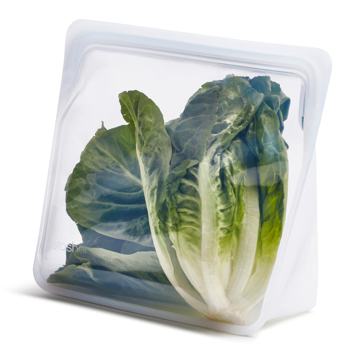 A reusable, transparent silicone storage bag containing a head of fresh green lettuce, standing upright on a white background.