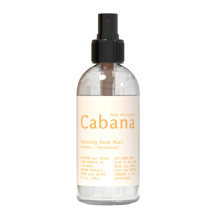 A clear spray bottle labeled “Cabana Relaxing Room Mist” with coconut and sandalwood scent, featuring minimalist design and light beige text on a white background. The bottle has a black spray top.