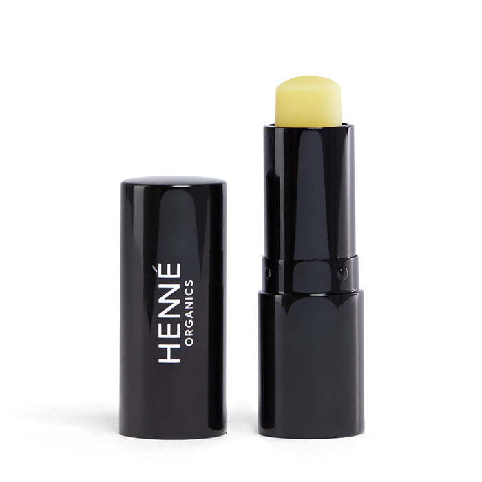 A black tube of Henné Organics lip balm with the cap removed and standing beside it, revealing the yellowish balm inside.