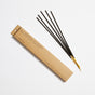 Four black incense sticks with yellow ends are placed next to a long, slim brown cardboard box labeled No. 29 Japanese Cedar by P.F. Candle Co. The box also notes there are 15 incense sticks inside.