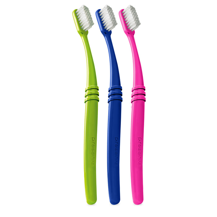 Three toothbrushes with white bristles, featuring green, blue, and pink handles, are standing upright side by side against a white background.