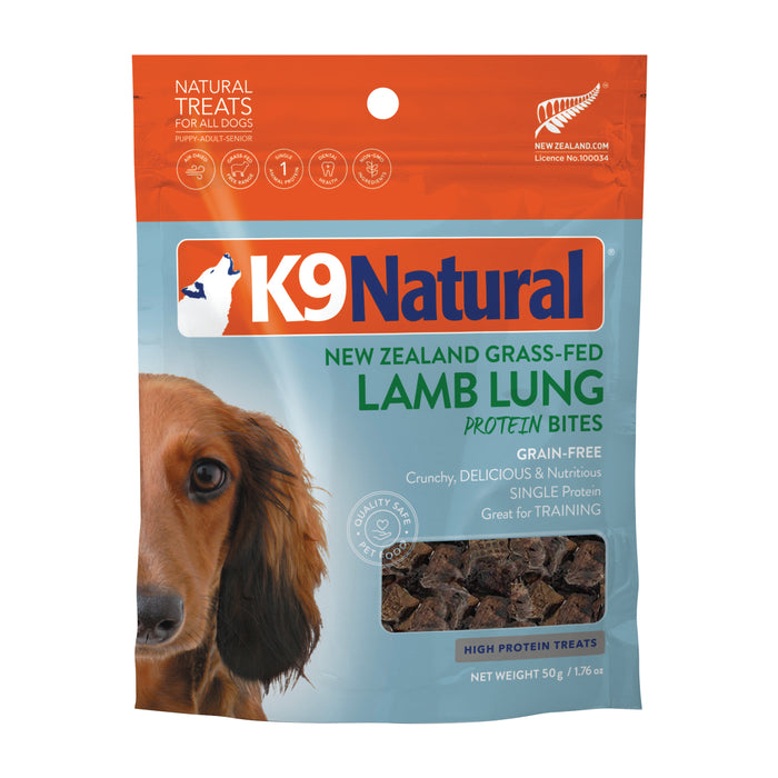 A bag of K9 Natural New Zealand Grass-Fed Lamb Lung Protein Bites dog treats. The packaging is orange and blue with an image of a dog, product details, and treats visible through a clear window.