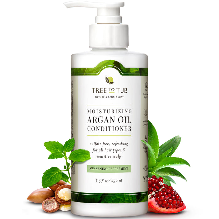 A bottle of Tree to Tub Moisturizing Argan Oil Conditioner with a pump top, surrounded by argan nuts, mint leaves, aloe vera, and a pomegranate, emphasizing its natural ingredients.