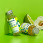 Two bottles of Grove Co. multi-purpose cleaner concentrate sit on a bright green surface, with one bottle upright and one lying down. A white rose and a green lemon wedge are placed beside them.