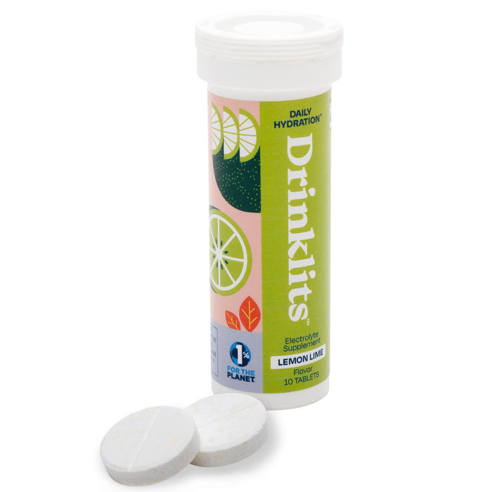 A tube of Drinklits electrolyte supplement tablets in lemon lime flavor, with a colorful label showing citrus illustrations. Two round white tablets are placed in front of the tube.
