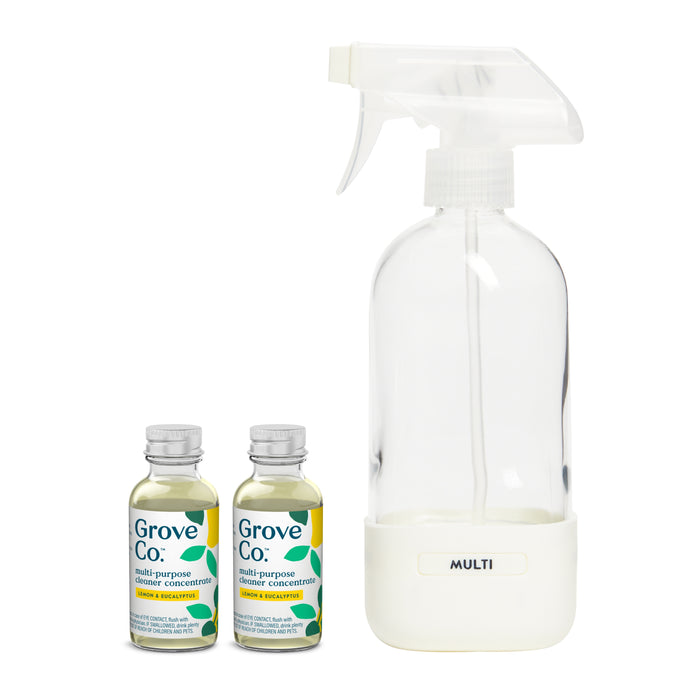 A clear spray bottle labeled Multi-Purpose Cleaner Starter Set sits beside two Grove Co. concentrate bottles with plant-based ingredients and an orange-rosemary scent. The transparent bottles feature eco-friendly green leaf designs, reflecting their sustainable packaging.