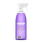 A clear spray bottle filled with purple liquid, featuring a white trigger nozzle and a white label with text and icons on the back, likely for a cleaning product.