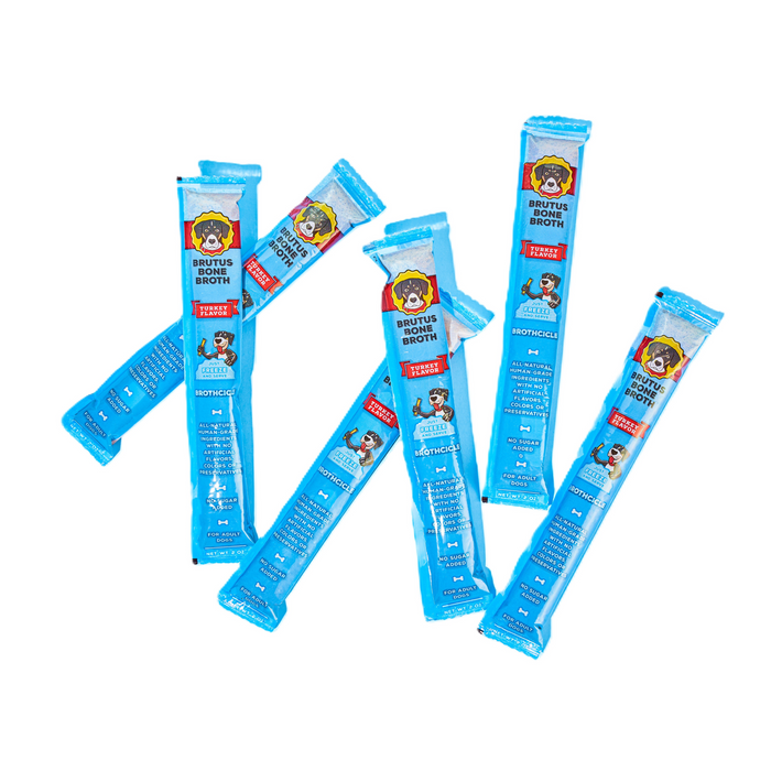 Six blue stick packs of Brutus Bone Broth for dogs are scattered on a white background. Each pack features a cartoon dog and product information in white and red text.