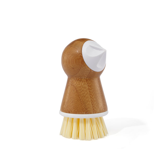 A wooden dish scrub brush with a rounded handle, a white plastic top, and stiff yellow bristles at the base, standing upright on a white background.