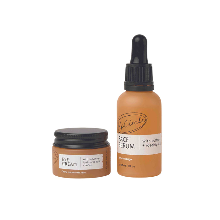 Two brown skincare containers: a small jar labeled Eye Cream with cucumber, hyaluronic acid + coffee and a bottle with a dropper labeled Face Serum with coffee + rosehip oil. Both have white and orange labels.