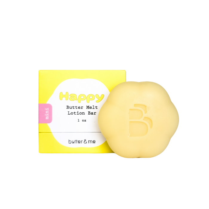 A yellow, flower-shaped lotion bar with a B embossed on it is placed next to its matching yellow and white box labeled Happy Butter Melt Lotion Bar 1 oz by butter & me.