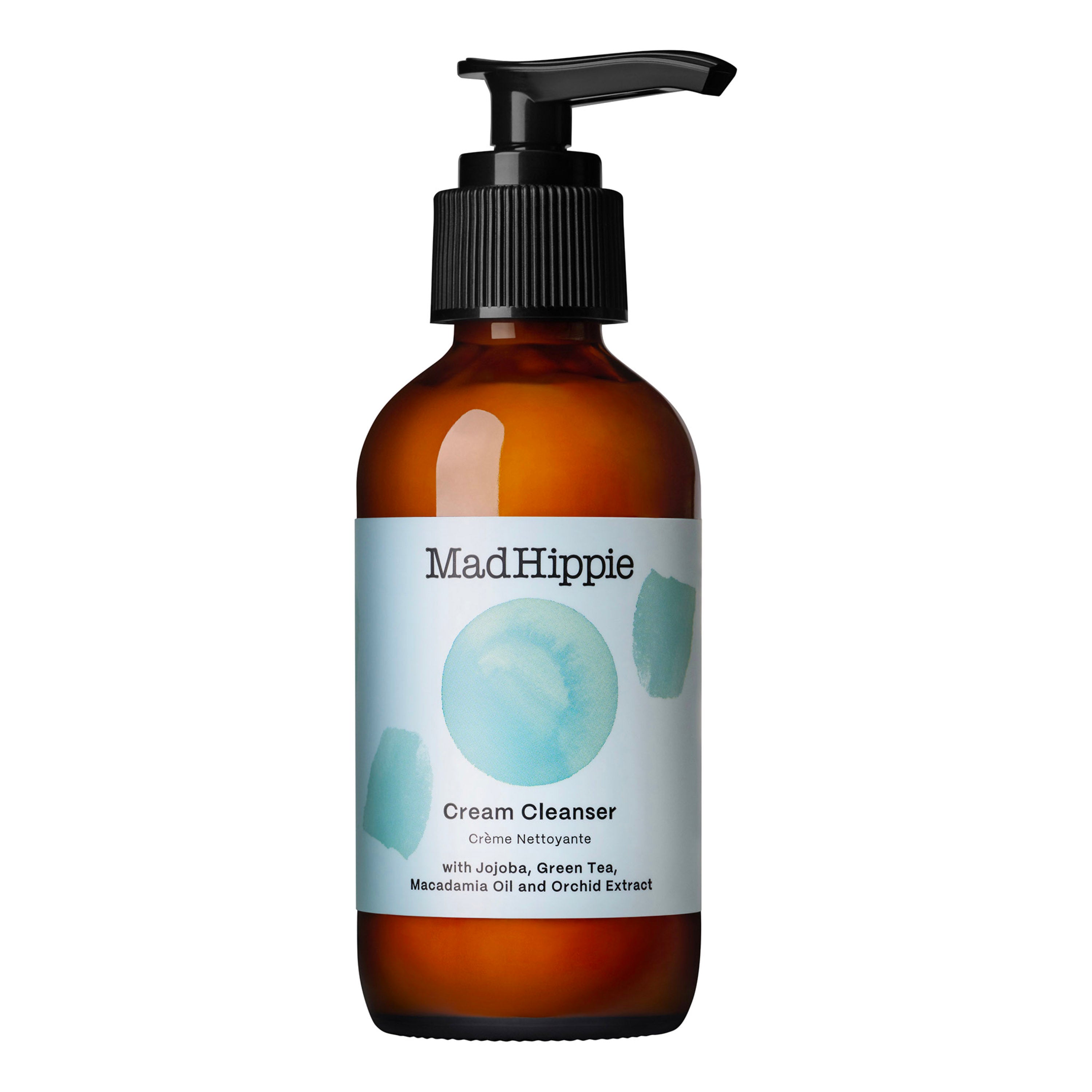 A brown pump bottle of Mad Hippie Cream Cleanser with a light blue label featuring teal watercolor circles lists ingredients like jojoba, green tea, macadamia oil, and orchid extract, all rich in antioxidants.