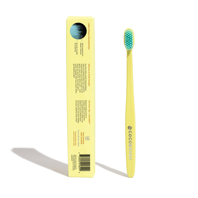 A yellow COCO BRUSH toothbrush with blue bristles stands upright next to its matching yellow box, which displays product information and a barcode, all on a white background.
