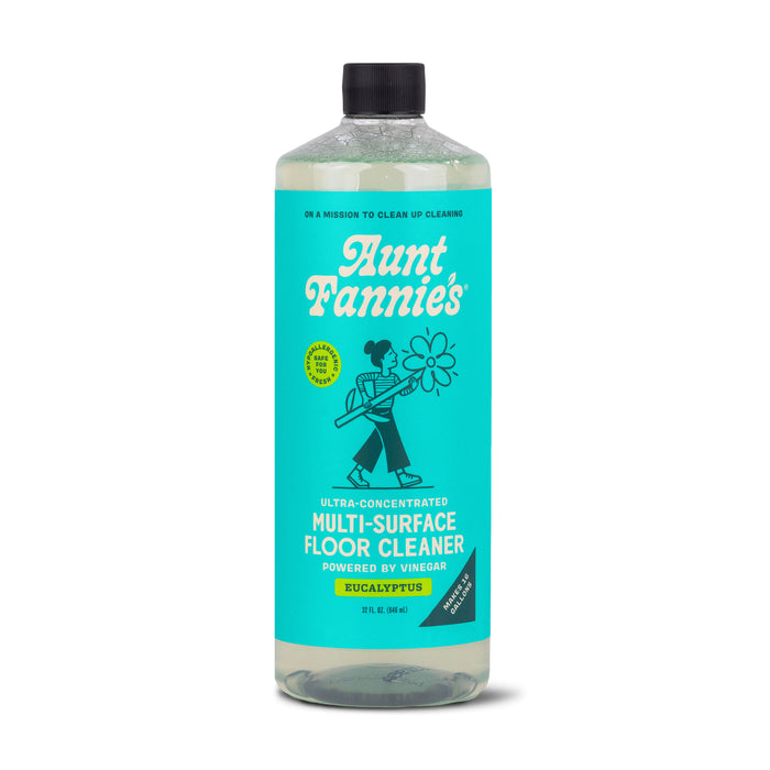 A bottle of Aunt Fannie’s Multi-Surface Floor Cleaner in eucalyptus scent. The bottle has a blue-green label with an illustration of a woman holding a mop and a large flower.