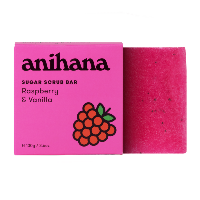 A bright pink box labeled anihana Sugar Scrub Bar Raspberry & Vanilla sits next to a matching pink sugar scrub bar with small dark specks. The box features a raspberry illustration.