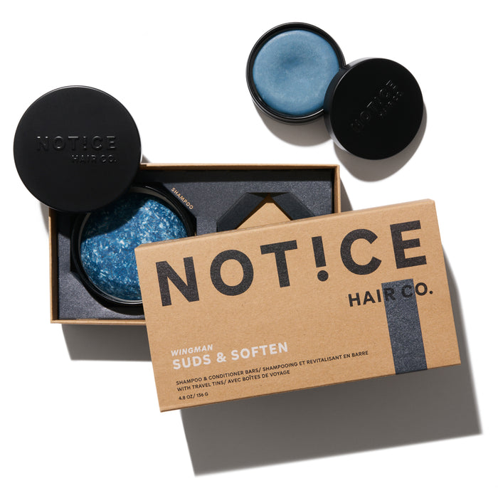 A cardboard box labeled NOT!CE HAIR CO. sits beside two open containers, each holding a round, blue solid bar. The packaging design is minimalist with black text and a modern aesthetic.