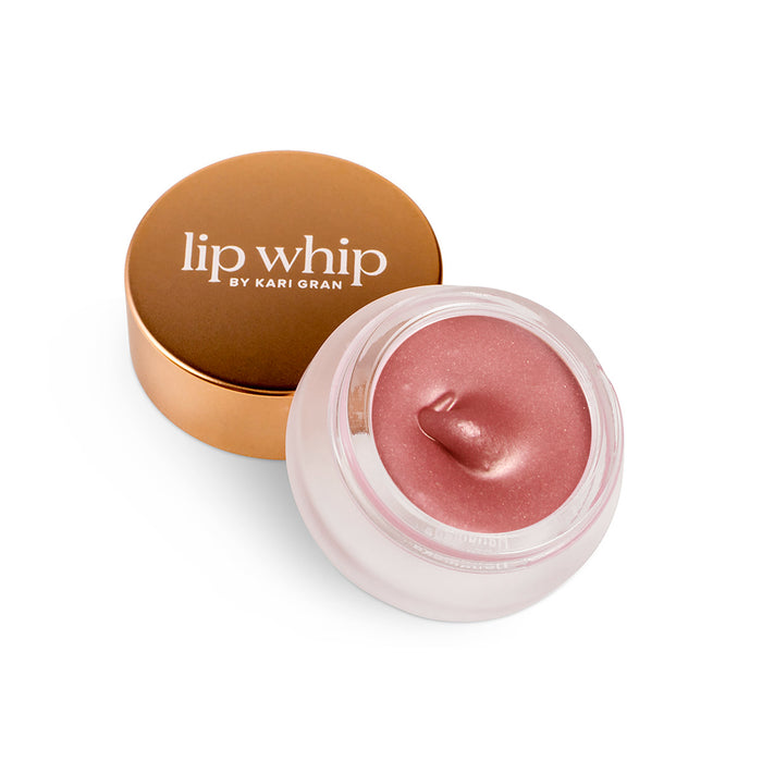A small round jar of shimmery pink lip balm with a rose gold lid labeled lip whip by Kari Gran, shown open with some product swirled on top.