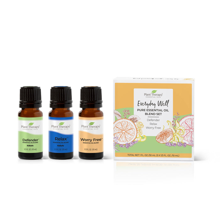 Three small amber bottles labeled “Defender,” “Relax,” and “Worry Free” of essential oils stand beside a Plant Therapy box labeled “Everyday Well Pure Essential Oil Blend Set” with fruit and leaf illustrations.
