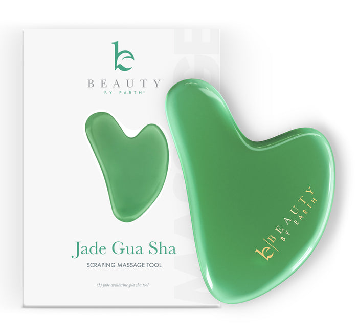 A green jade gua sha tool with the gold Beauty by Earth logo is placed in front of its matching white packaging, which shows an image of the tool and the text Jade Gua Sha Scraping Massage Tool.