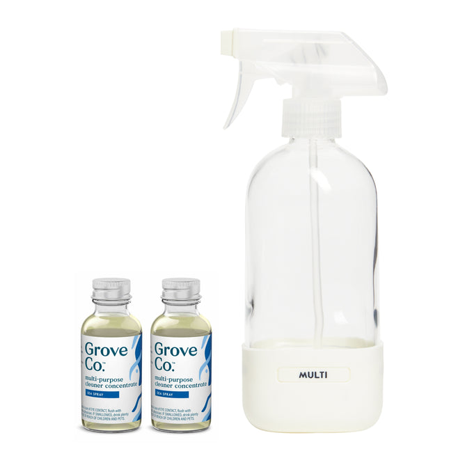 A clear MULTI spray bottle is next to two Grove Co. Multi-Purpose Cleaner Starter Set concentrate bottles, featuring sustainable packaging with blue labels and twist-off caps, containing a powerful plant-based formula.