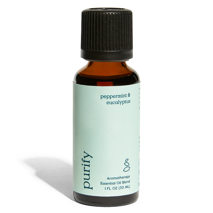 A small amber glass bottle with a black cap labeled “purify” containing peppermint & eucalyptus aromatherapy essential oil blend, 1 fl oz (30 ml). The label is light green with minimalist design.