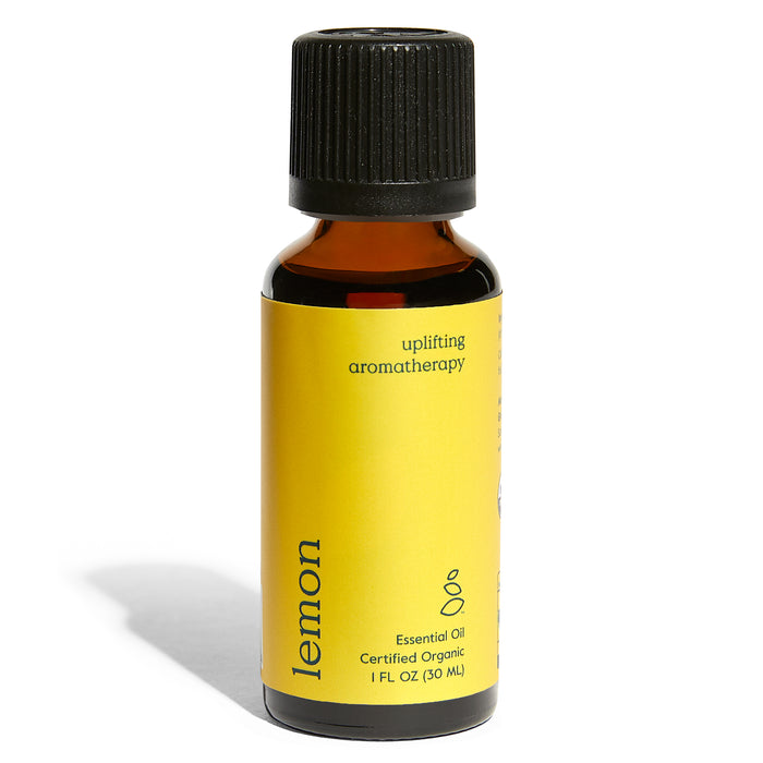 A small amber glass bottle with a black cap and a bright yellow label reading “lemon,” “uplifting aromatherapy,” and “essential oil certified organic 1 FL OZ (30 mL).”.