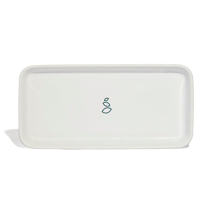A rectangular white ceramic tray with rounded edges, featuring a simple green minimalist design of three shapes—two ovals and a small circle—in the center.