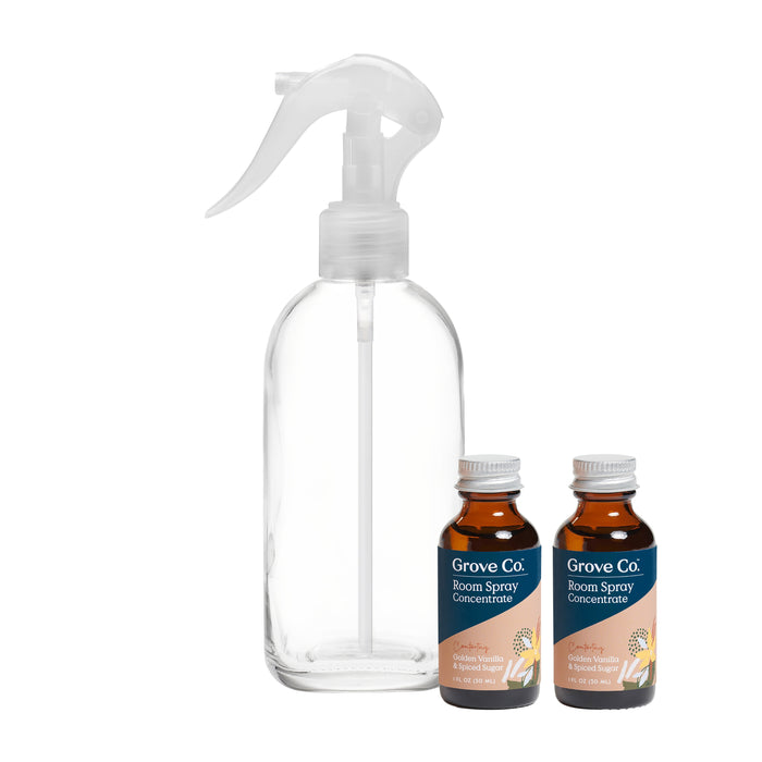 A clear, empty spray bottle with a white trigger is shown next to two small brown bottles labeled Grove Co. Room Spray Concentrate with citrus illustrations on the labels.