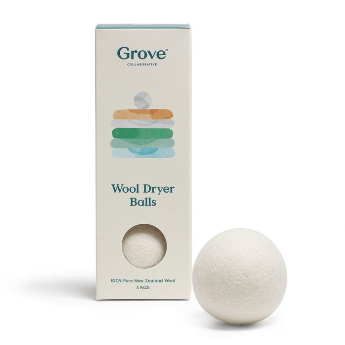 A box labeled Grove Wool Dryer Balls stands next to a single white wool dryer ball. The box is off-white with colorful stacked shapes and a circular cutout showing the ball inside.