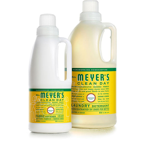 Two bottles from Mrs. Meyers Laundry Detergent & Fabric Softener Set are displayed. The Basil-scented detergent handles 64 loads, while the Honeysuckle fabric softener covers 32. Both feature yellow labels with green and white text.