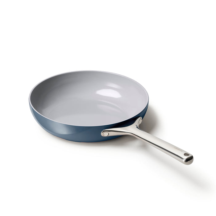 A blue frying pan with a white nonstick interior and a long silver handle is placed on a white surface.