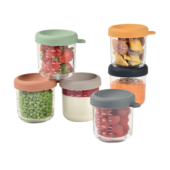 Six BEABA Glass Baby Food Jars, each with a colorful lid, are filled with strawberries, fruit slices, peas, white sauce, raspberries, and orange puree. Theyre stacked in a small pyramid against a white background—ideal for storing homemade baby food!.