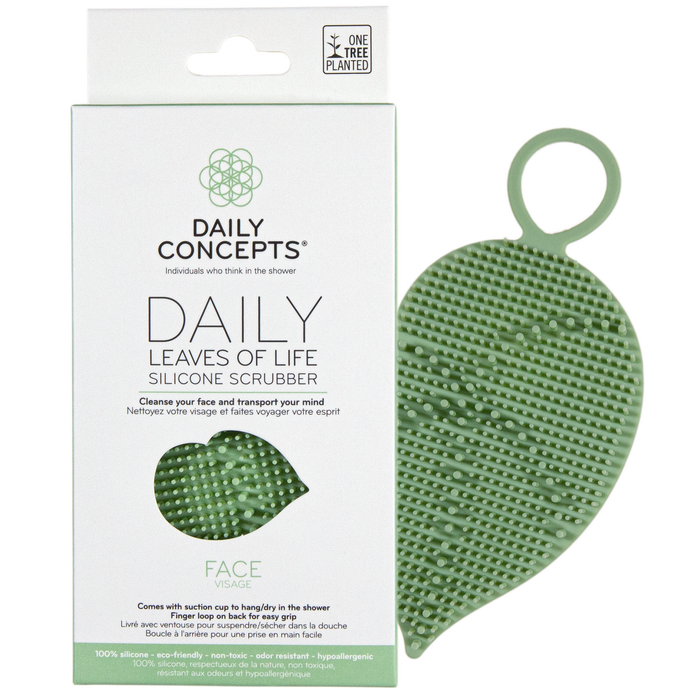 A green, leaf-shaped silicone face scrubber is displayed next to its white and green packaging, labeled Daily Concepts Daily Leaves of Life Silicone Scrubber for face cleansing.