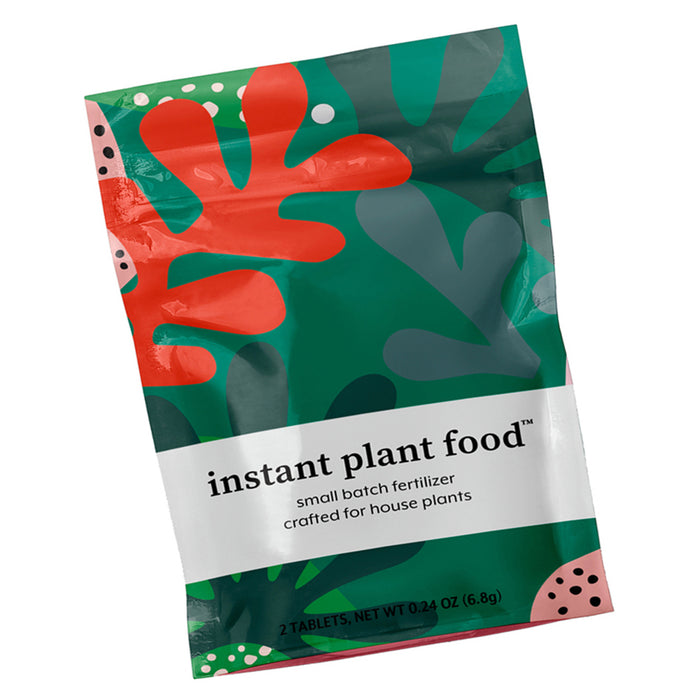 A vibrant packet labeled Instant Plant Food Tablets by Instant Plant Food features bold green and orange abstract plant shapes, containing expertly crafted small batch fertilizer designed to deliver essential nutrients for nourishing your indoor plants.