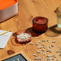 Small plastic letters are scattered on a wooden table near two transparent storage containers, a glass of water, a notepad with a pencil, and a letter board in the corner. Warm sunlight lights the scene.