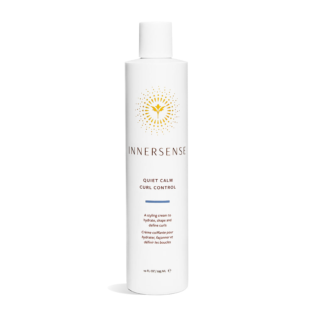 A white bottle of Quiet Calm Curl Control by Innersense Organic Beauty is shown against a plain background, featuring a yellow logo and text. Its described as the perfect solution to hydrate curls and effortlessly tame frizz.