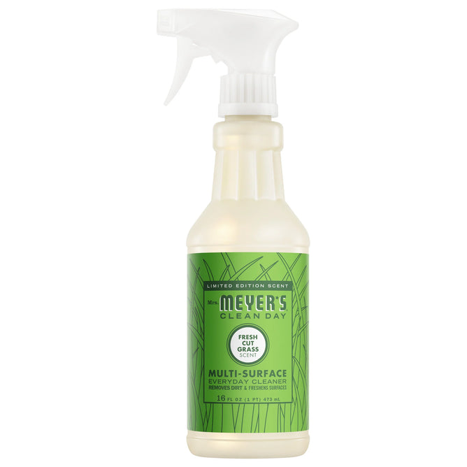 A bottle of Mrs. Meyer's Multi-Surface Cleaner in Fresh Cut Grass scent features a green label with grass designs and a white spray nozzle, bringing a fresh essential oil fragrance to your space with every spray.