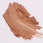 A smooth, medium brown makeup swatch smeared on a white background, showing a creamy texture with visible brush strokes.