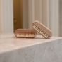 Two beige PAUME Hand & Nail Brushes with natural boar bristles rest on a marble surface. One displays its rejuvenating bristles while the other stands upright, showcasing the PAUME logo, set against a blurred vertical line background that enhances their luxurious hand care appeal.