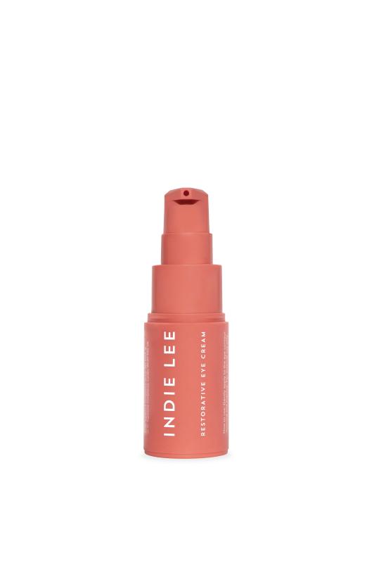 A coral-colored pump bottle labeled Indie Lee Restorative Eye Cream stands upright against a plain white background.