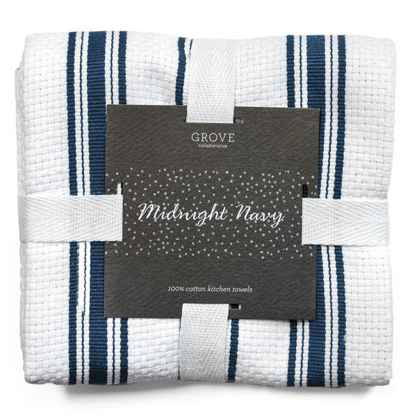 A bundle of Grove Co. Organic Cotton Classic Kitchen Towels is secured with white straps, featuring navy and black stripes on a white background. A dark label reads Midnight Navy and 100% cotton kitchen towels, adding elegance to these essential cleaning accessories.