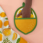 A hand slips into The Neighborgoods Pot Holder - Lemon on a peach surface beside a lemon-patterned towel—an irresistible kitchen essential for any home chef.