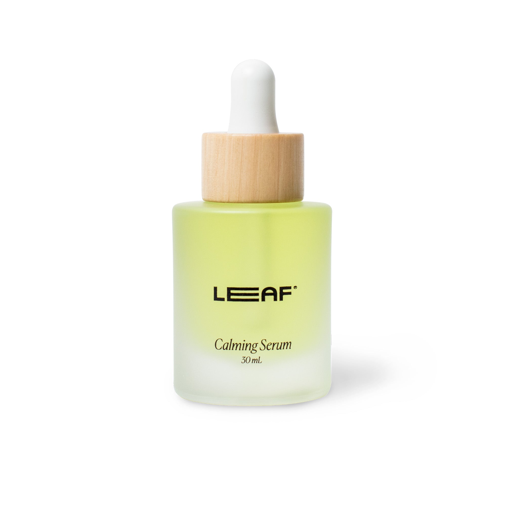 The 30 ml Calming Serum w/ Dropper by Leaf Shave features a frosted glass bottle, wooden cap, and black printed label. Its skin-soothing antioxidants and light green hue stand out against a pristine white background.