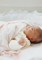 A baby lies in a white bassinet covered by a soft, pale pink Little Love Blanket - Cloud.