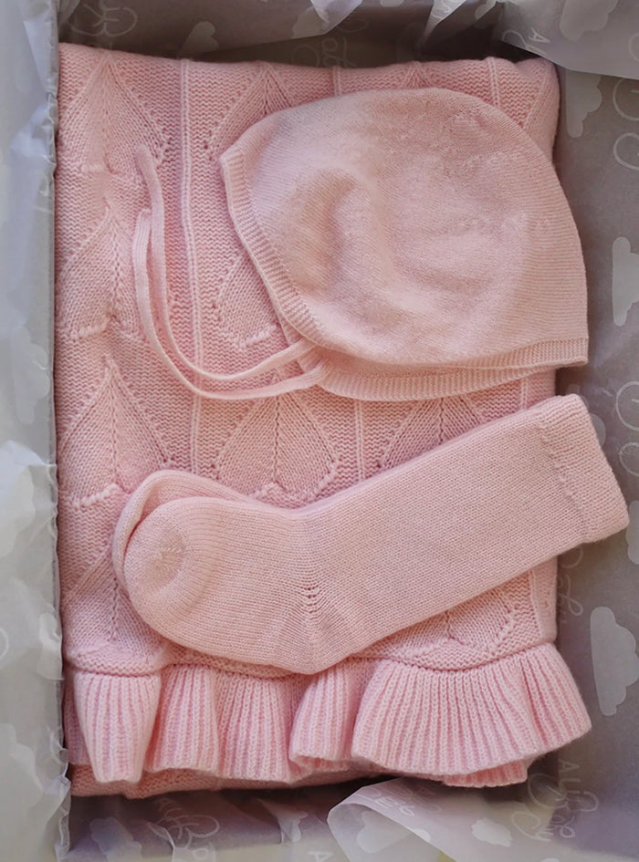 AU Baby Cashmere Cloud Baby Blanket Gift Set in Peony Pink, featuring a light pink organic cashmere blanket with a ruffled edge, a bonnet with ties, and a pair of socks, packaged in a gift box.