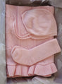 AU Baby Cashmere Cloud Baby Blanket Gift Set in Peony Pink, featuring a light pink organic cashmere blanket with a ruffled edge, a bonnet with ties, and a pair of socks, packaged in a gift box.
