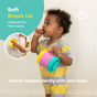 A toddler in a yellow and gray striped outfit holds a colorful snack cup and eats a snack. Text reads Soft Snack Lid, Designed for little hands, Snack independently with less mess. Inset shows the snack cup lid.