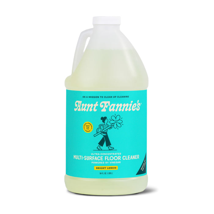 A large plastic jug of Aunt Fannie’s Multi-Surface Floor Cleaner with a turquoise label featuring a person holding a flower. The label text highlights that it is ultra-concentrated, powered by vinegar, and Bright Lemon scented.