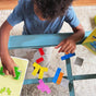 A young child arranges HABAs Logic! GAMES: Happy Worms, made from sustainably sourced wood, on a glass table. Nearby are the games box and green activity sheet for more brain-boosting logic games. Suitable for ages 5+.